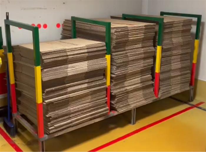 Racks de cartón organizados por código de color sobre piso demarcado en amarillo y rojo